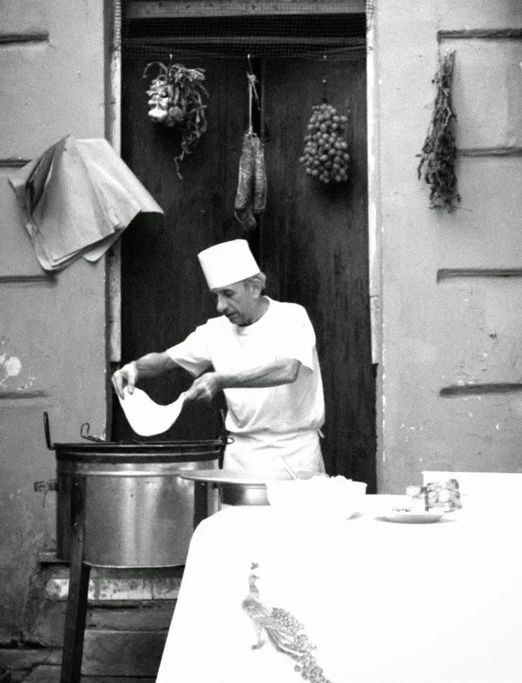 Un uomo prepara l'impasto davanti a una porta, in una fotografia in bianco e nero