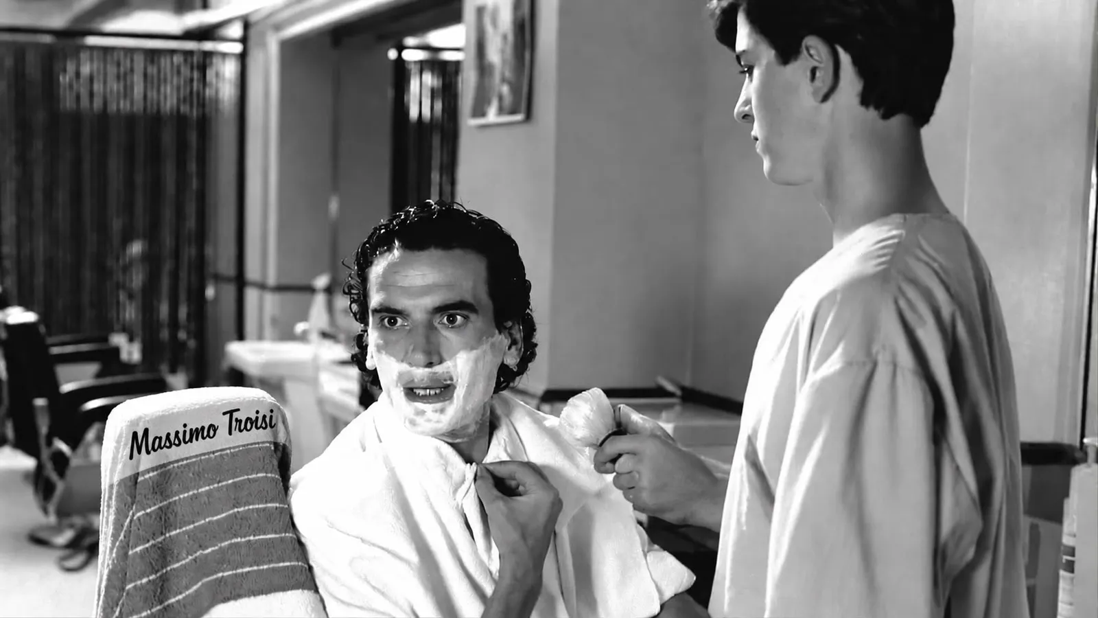 Scena dal barbiere in bianco e nero con il nome Massimo Troisi sull'asciugamano